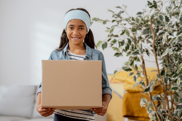 La dolce ragazza aiuta i suoi genitori durante il trasloco trasporta le cose dalla stanza imballate in una scatola di cartone trasporta scatole che si trasferiscono nell'affitto di un condominio