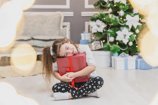 La dolce ragazza con la coda di cavallo sta dormendo su un grande regalo di Natale che sembra fantastico