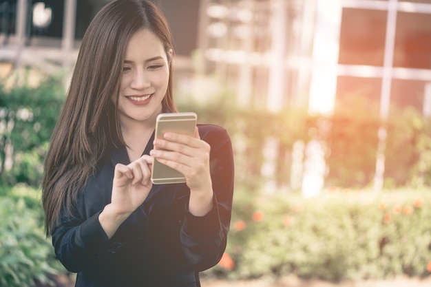 La donna abbastanza asiatica sta mandando un sms sul cellulare nel parco della città