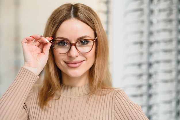 La donna abbastanza giovane sta scegliendo nuovi occhiali al negozio di ottica