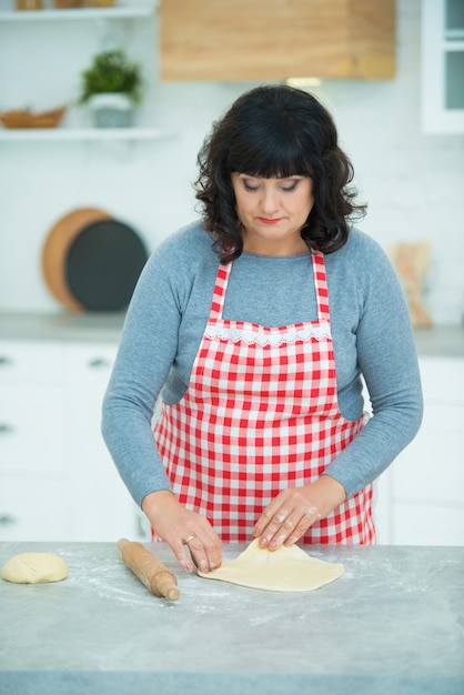 La donna abbastanza matura stende scolpisce la pasta con un mattarello in cucina sul tavolo. Nonna casalinga.