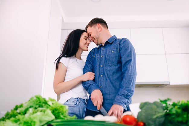 La donna abbraccia il marito mentre prepara le verdure per l'insalata in cucina.