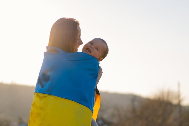 La donna abbraccia il suo piccolo figlio avvolto nella bandiera gialla e blu dell'ucraina all'aperto