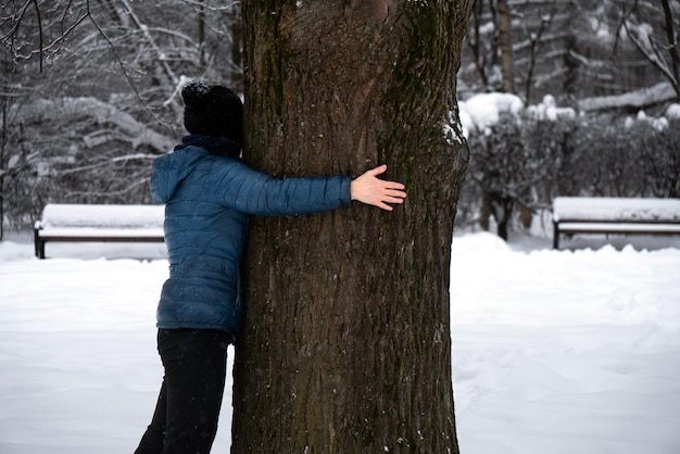 La donna abbraccia un tronco di una grande vecchia quercia in un parco invernale innevato nella stagione fredda