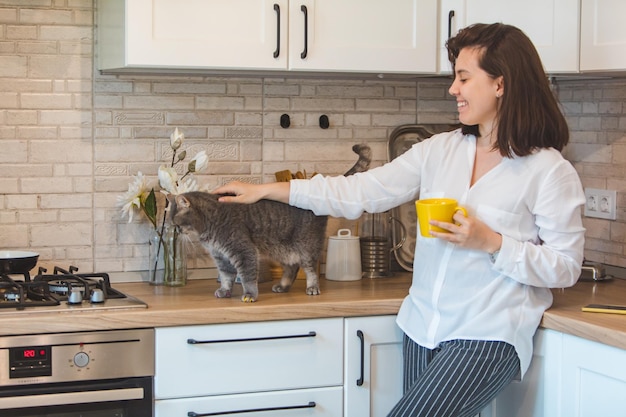 La donna accarezza il gatto e beve il tè in cucina