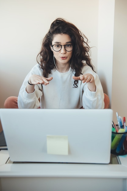 La donna adorabile sta spiegando qualcosa al computer portatile mentre ha lezione in linea a casa