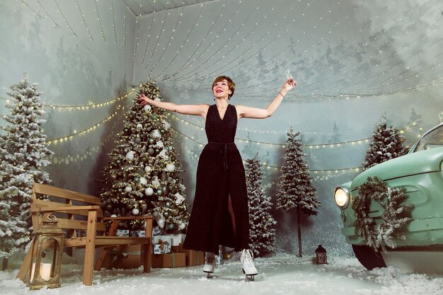 La donna adulta beve champagne su una pista di pattinaggio a Capodanno mentre pattina accanto a un albero di Natale