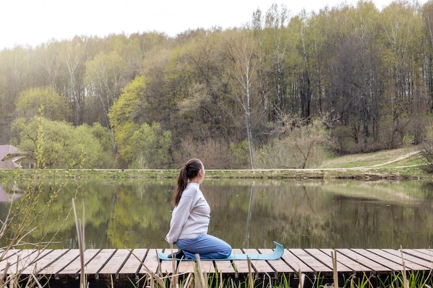 La donna adulta fa yoga sul lago nel parco