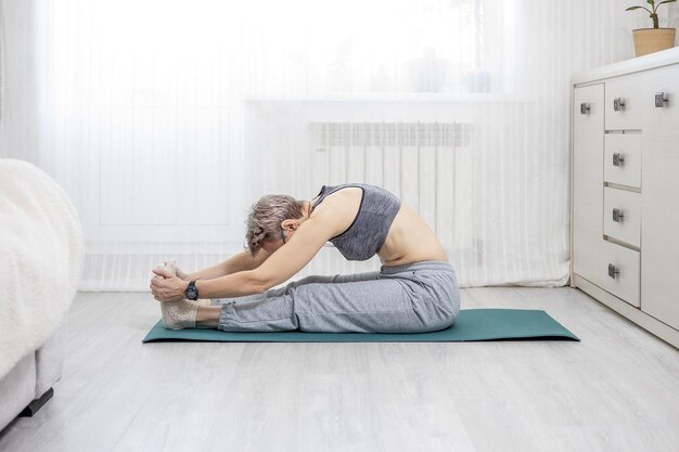 La donna adulta in abbigliamento sportivo è impegnata nello stretching a casa