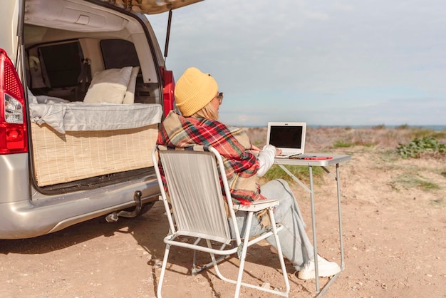 La donna adulta lavora su un computer portatile mentre viaggia con il camper Concetto di stile di vita delle persone moderne in smart working o libertà dei nomadi digitali