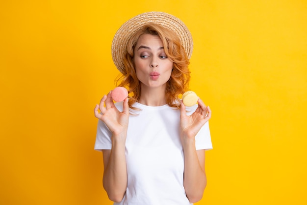 La donna affascinante vuole mordere il gustoso macaron che tiene il macaron vicino alla ragazza di bellezza della bocca aperta che gode dei dolci