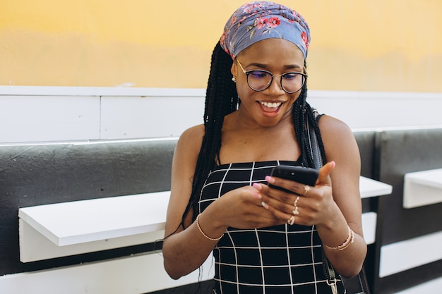 La donna afroamericana in un vestito si diverte a guardare fuori nel telefono e sorridere