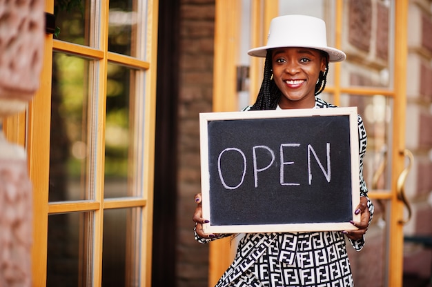 La donna afroamericana tiene aperta il cartello di benvenuto nella moderna caffetteria caffetteria pronta al servizio, ristorante, negozio al dettaglio, proprietario di una piccola impresa.