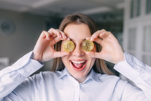 La donna alla moda in giacca e cravatta si diverte con due monete bitcoin sorridendo e felice