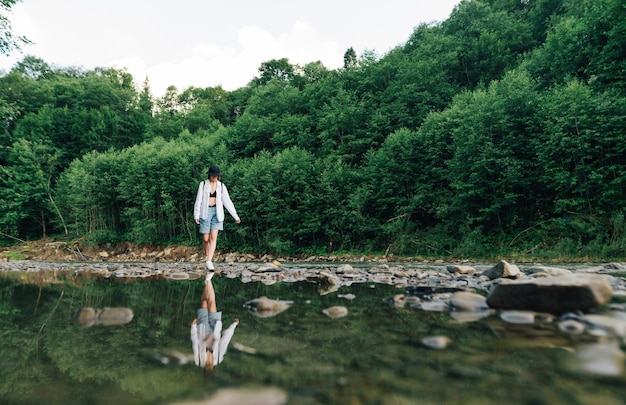 La donna alla moda in un cappello cammina con attenzione sulle pietre sul fiume