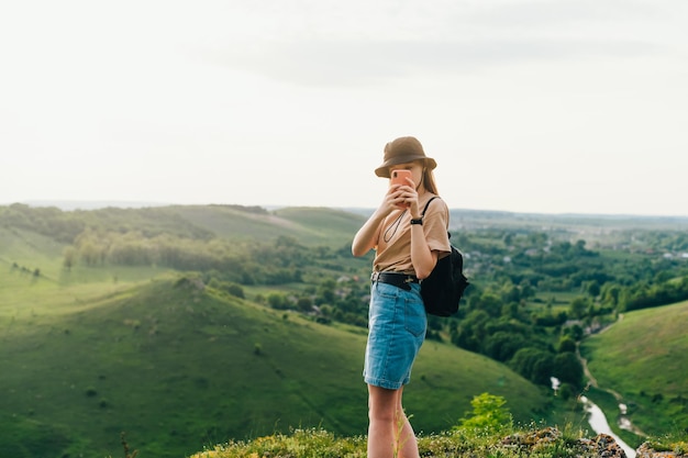 La donna alla moda si trova sul bordo della montagna su uno sfondo di uno splendido scenario e utilizza uno smartphone Il turista hipster della ragazza è impegnato nel turismo domestico Zakupne Tovtry