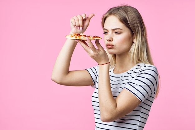 La donna allegra con il fast food nelle sue mani fa uno spuntino delizioso sfondo rosa