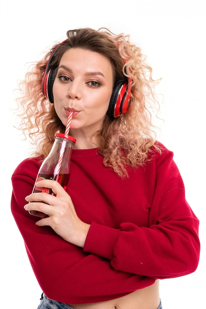 La donna allegra con le cuffie rosse ascolta musica e ingoia il succo