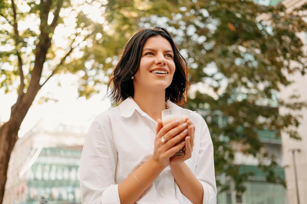 La donna allegra gode del tempo soleggiato sulla strada con una tazza di caffè