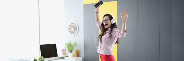 La donna allegra in cuffie con lo smartphone sta ballando sul divano