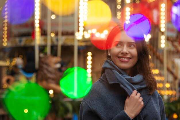 La donna allegra indossa un cappotto grigio che cammina per strada con luce bokeh. Spazio vuoto