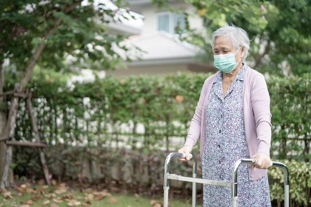 La donna anziana asiatica cammina con il deambulatore e indossa una maschera per proteggere il Covid Coronavirus