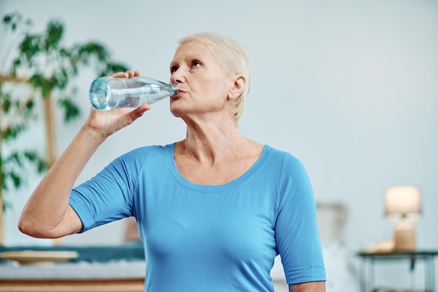 La donna anziana beve l'acqua dopo un concetto di allenamento mattutino di uno stile di vita sano