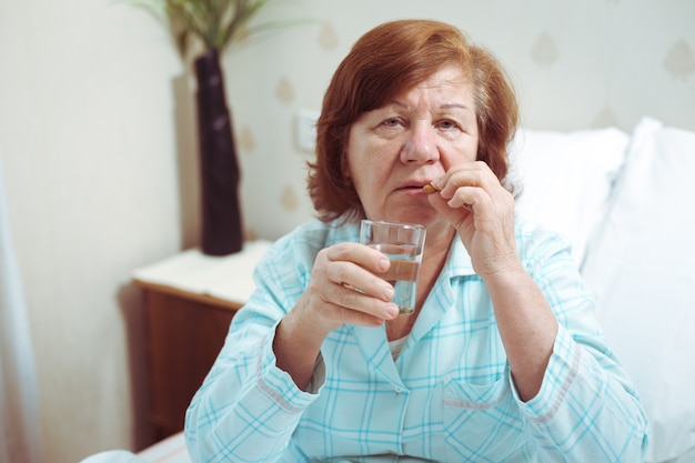 La donna anziana beve la medicina a letto, la persona anziana sola ha preso un'influenza.