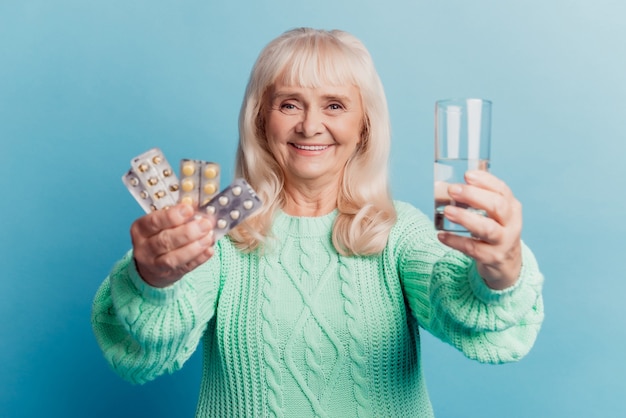 La donna anziana con l'acqua del prodotto medico tiene le compresse in mano su sfondo blu