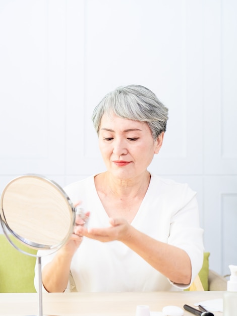 La donna anziana dell'Asia sta spruzzando il profumo a casa.