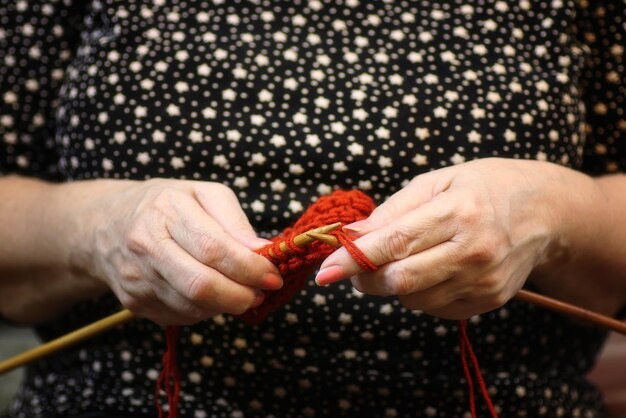 La donna anziana è impegnata a lavorare a maglia maglioni caldi per i suoi nipoti