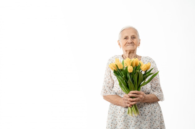 la donna anziana in abito bianco tiene in mano fiori gialli