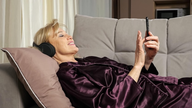 La donna anziana legge le notizie ascoltando la musica tramite le cuffie