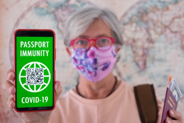 La donna anziana sfocata mostra l'app per il passaporto sanitario digitale del telefono cellulare con pass verde per le persone vaccinate