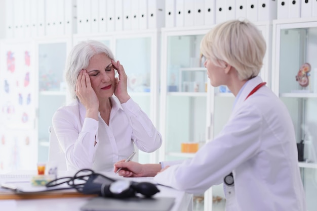 La donna anziana si lamenta di una forte emicrania al medico nel gabinetto dell'ospedale, la signora terapista ascolta