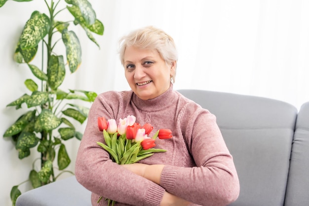 La donna anziana si siede sul sofà con il mazzo dei tulipani. Festa della mamma.