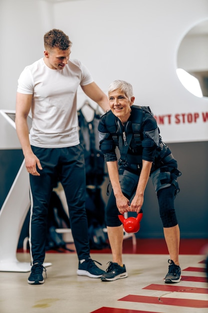 La donna anziana sta facendo l'allenamento EMS con il personal trainer in palestra.