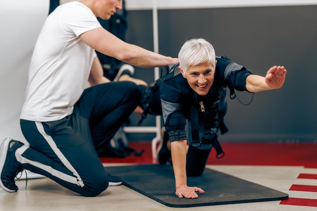 La donna anziana sta facendo l'allenamento EMS con il personal trainer in palestra.