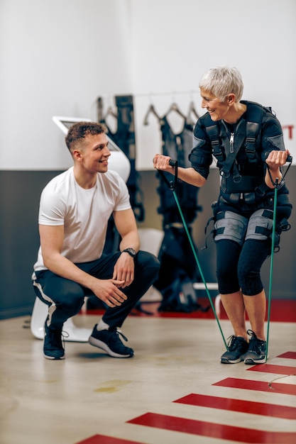 La donna anziana sta facendo l'allenamento EMS con il personal trainer in palestra.