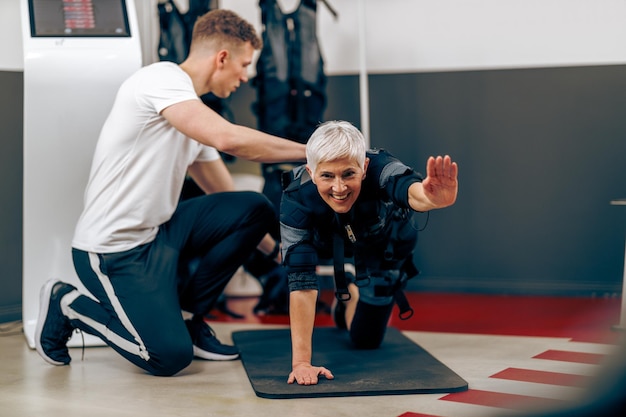 La donna anziana sta facendo l'allenamento EMS con il personal trainer in palestra.