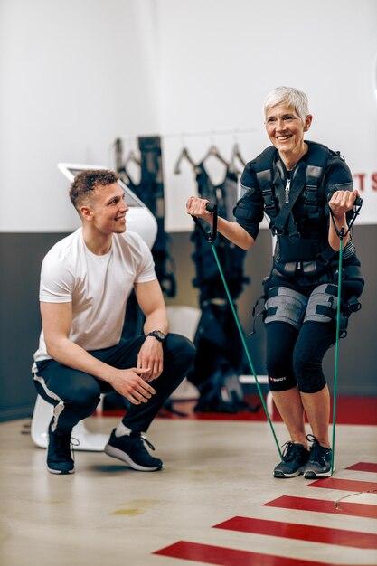 La donna anziana sta facendo l'allenamento EMS con il personal trainer in palestra.