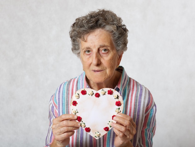La donna anziana tra i 70 e gli 80 anni tiene il cuore nelle mani. Sfondo grigio