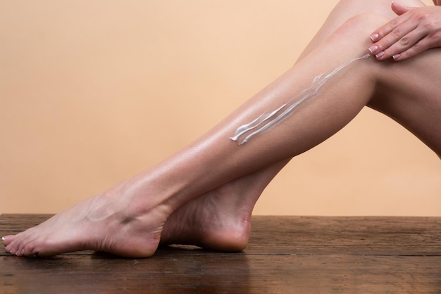 La donna applica la lozione alla crema cosmetica della gamba della pelle sulla gamba della donna con la pelle morbida pulita che applica l'idratazione...