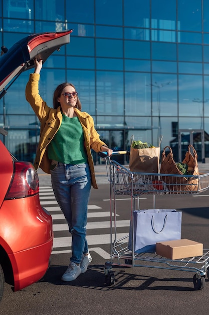 La donna apre il bagagliaio dell'auto e tiene il carrello con la spesa