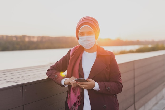 La donna araba musulmana indossa l'hijab e la maschera medica protettiva blu che scorre internet blog social network affari e concetto di videochiamata