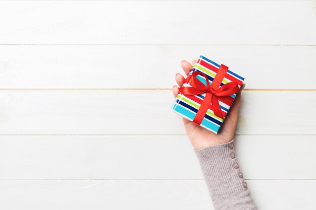 La donna arma il contenitore di regalo della tenuta con il nastro colorato sul fondo di legno bianco della tavola, sulla vista superiore e sullo spazio della copia