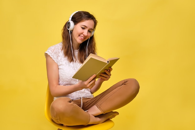 La donna ascolta in modo astratto un audiolibro in cuffia collegato al libro e lo guarda.