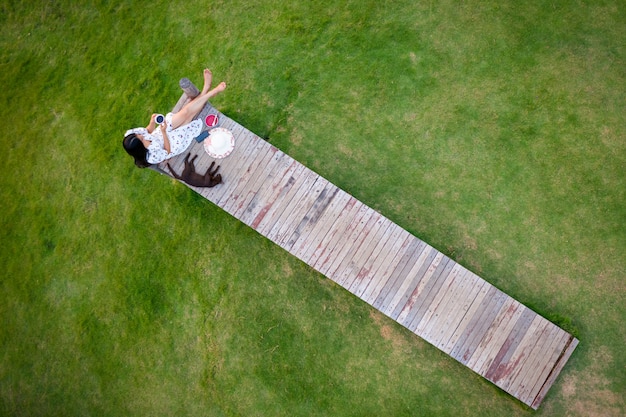 La donna asiatica che si siede sul ponte di legno nell'antenna verde del giardino rivaleggia