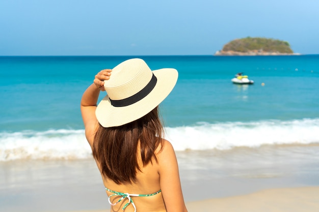 La donna asiatica del viaggiatore felice in bikini con il cappello della spiaggia gode alla spiaggia tropicale in vacanza. Estate sul concetto di spiaggia.