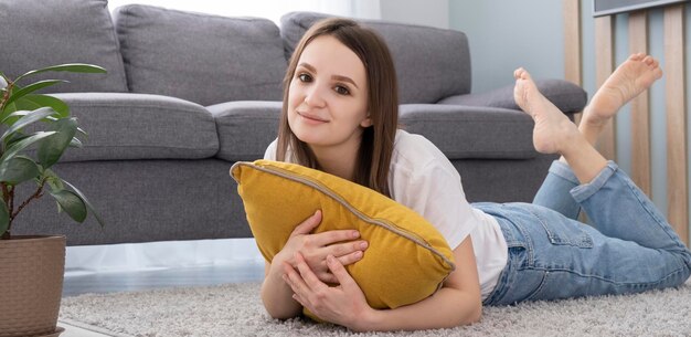 La donna asiatica felice dello stile di vita domestico si rilassa sdraiata sui cuscini del pavimento del soggiorno che si rilassano